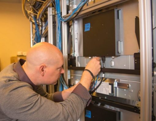 Audio visual technician checking cables on the back of a large array of LCD panels